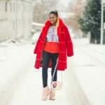 Fashion-forward woman wearing a red coat striding down a snow-covered street, exuding style and confidence.