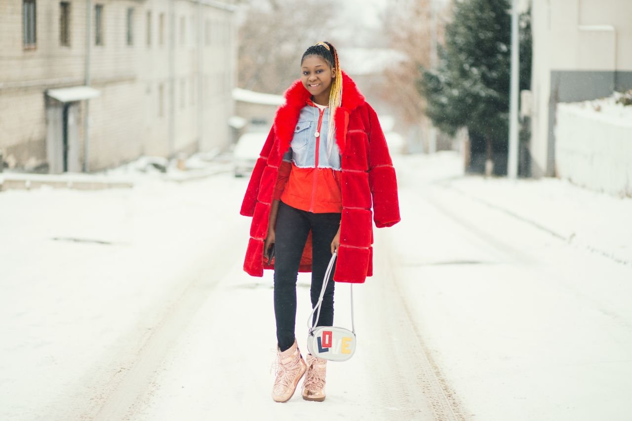 Fashion-forward woman wearing a red coat striding down a snow-covered street, exuding style and confidence.