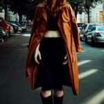 Fashionable woman in trench coat strolls down a Berlin street, exuding urban style.